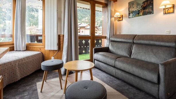 En hyggelig stue med sofa, to skarmuer, et lille bord og en seng med mønstret dyne.