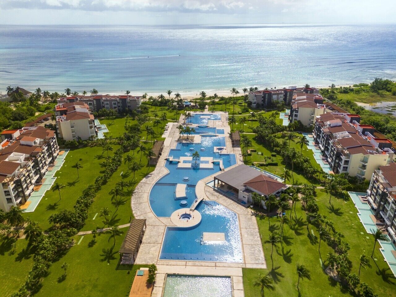 A resort with multiple swimming pools, a central water feature, and beachfront views.
