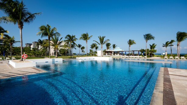 Una grande piscina all'aperto con acqua cristallina, circondata da palme e un'area relax coperta.