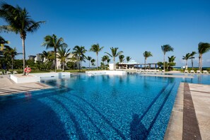 A large outdoor swimming pool with clear blue water, surrounded by palm trees and a covered seating area. - Ocean front resort, Andalucia Mareazul, Private Walkout pool (Playa del Carmen)