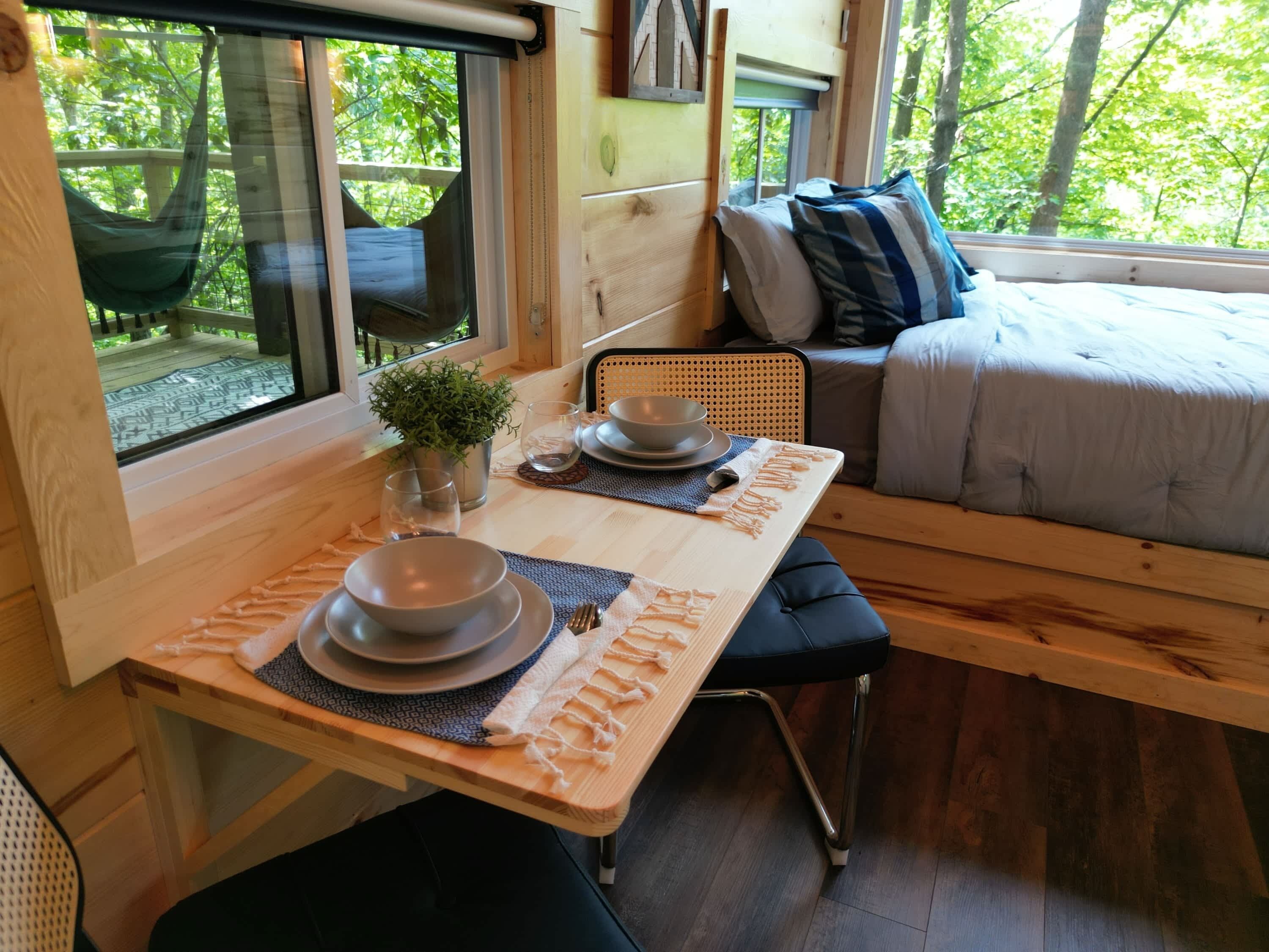 A cozy room with a dining table set for two, a bed with a view of the outdoors, and a hammock outside.