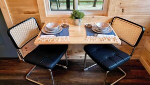 Een houten eettafel met twee zwarte lederen stoelen, een kleine potplant en een raam met uitzicht op bomen.