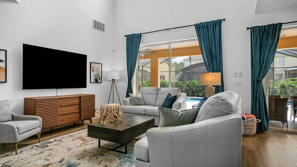 Una sala de estar moderna con un televisor de pantalla plana grande, un sofá gris, un mueble de madera y una mesa de centro.