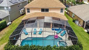 Un jardin avec une piscine, délimité par une clôture en verre, et agrémenté de chaises longues et d’un flotteur en forme de flamant rose.