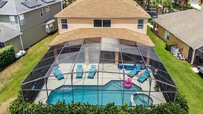 A backyard with a swimming pool, enclosed by a glass fence, and surrounded by lawn chairs and a pink flamingo float.