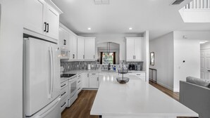 A modern kitchen with white cabinetry, a central island, and a view to the living area. - Avatar | 2.5 Mi Disney | Pool | Game Room 8510 (Kissimmee)