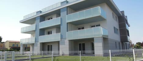 A modern multi-story building with balconies, a fenced courtyard, and a flat roof.