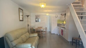 Ein Wohnzimmer mit einer Couch, einem Esstisch, Stühlen, einer Küche mit Schränken und einer Spüle sowie einer Treppe.