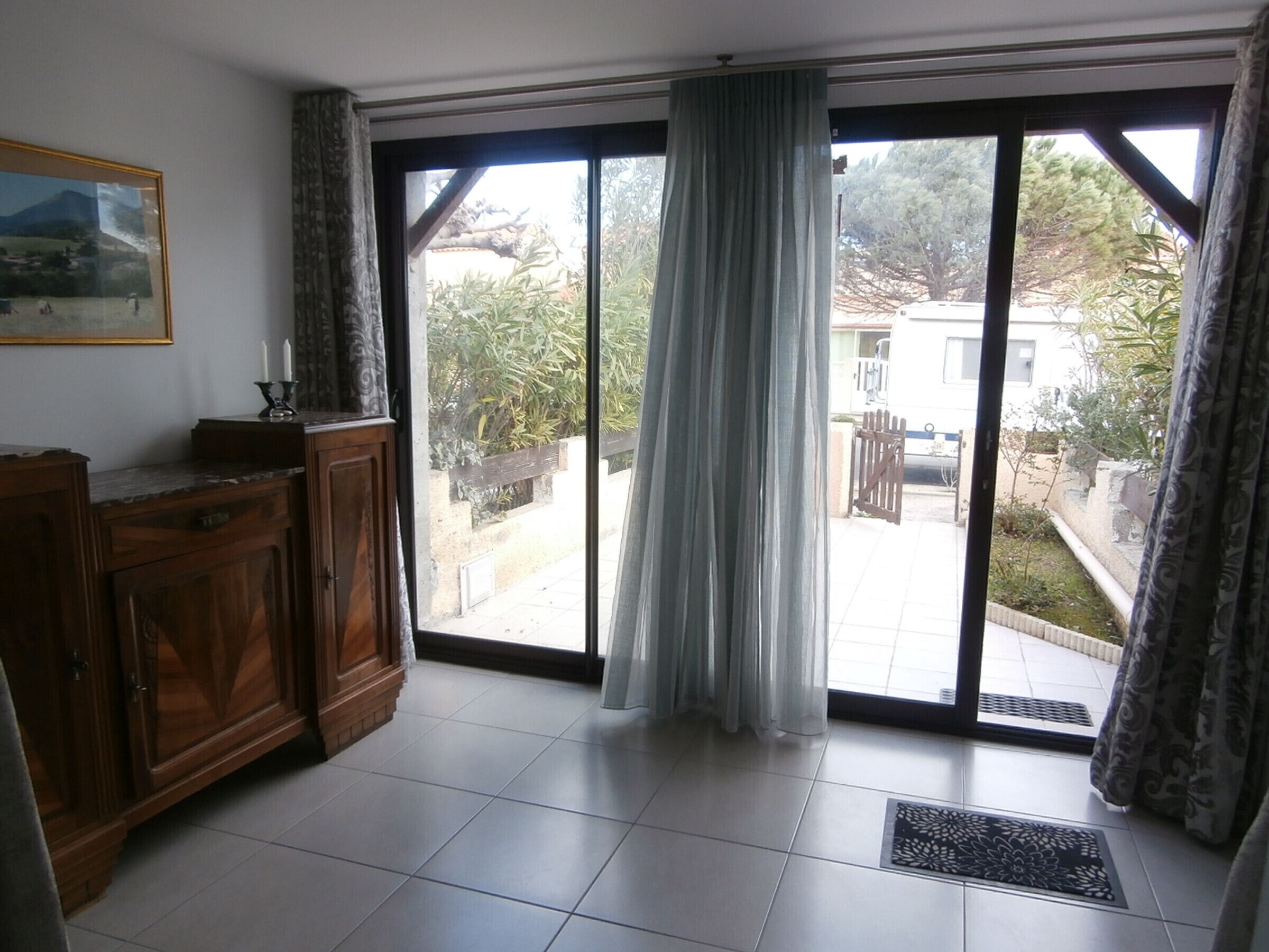 Una habitación con una puerta corrediza de vidrio que da a un patio, un mueble de madera y un cuadro en la pared.