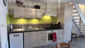 Eine moderne Küche mit Geschirrspüler, Backofen und Kaffeemaschine. Eine Treppe führt zu einer weiteren Ebene.