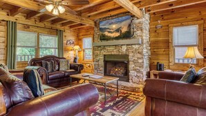 A cozy cabin interior with leather sofas, a fireplace, and a ceiling fan. - View To Remember, Stunning Mountain Views, Hot Tub, Game Room, Near Pigeon Forge (Sevierville)