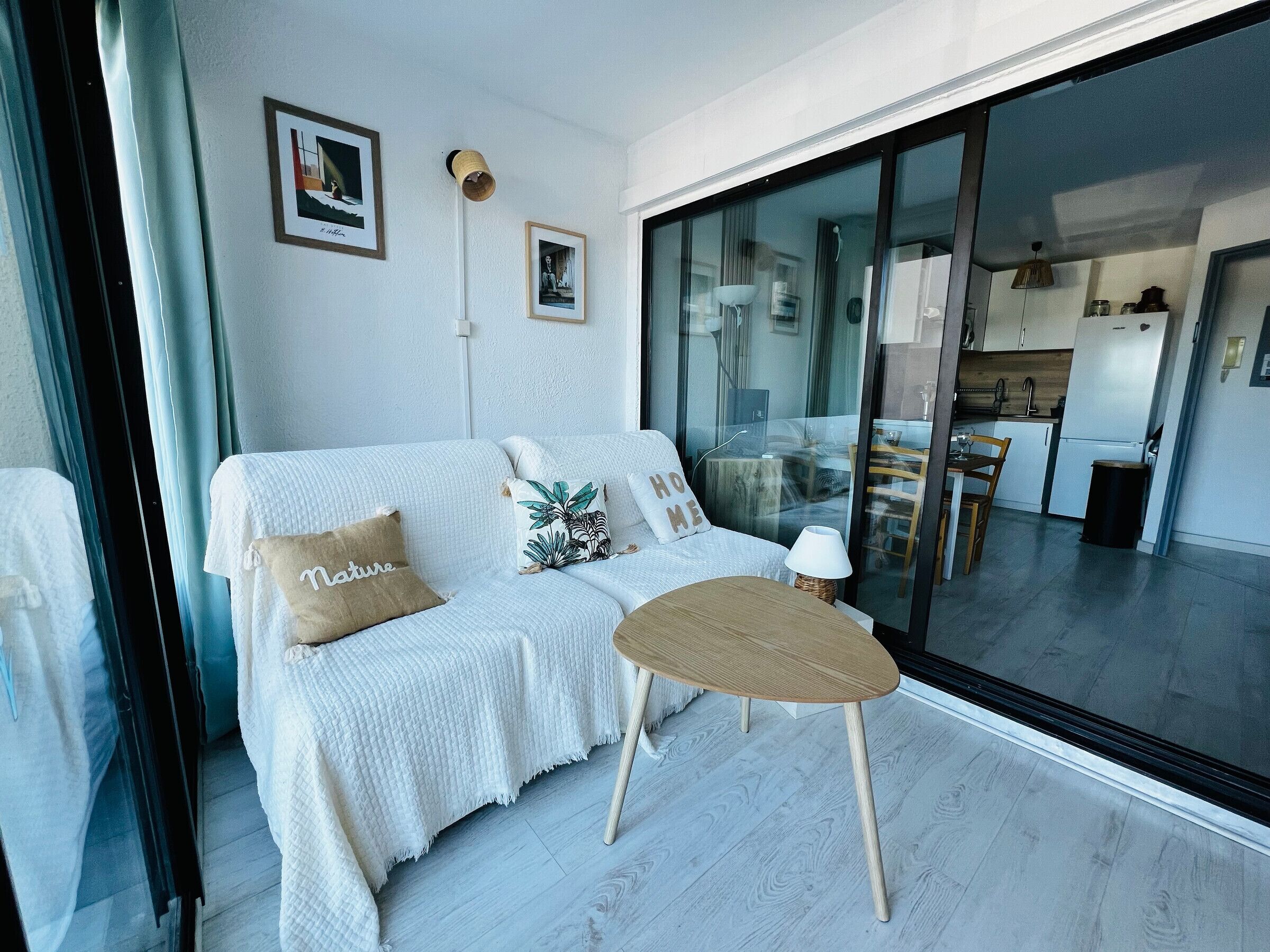 A modern living room with a white sofa, a small round table, and a glass door leading to a kitchen.