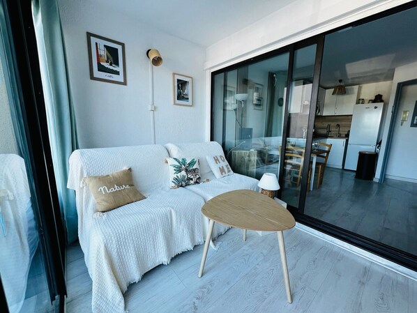 A modern living room with a white sofa, a small round table, and a glass door leading to a kitchen.
