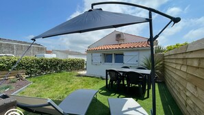 En uteplats med ett bord och stolar, en möblerad sittgrupp under tak och ett hus med ett tegeltak i bakgrunden.