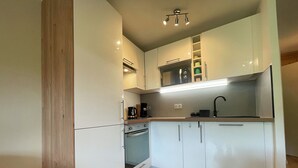 Una cocina compacta con armarios blancos, horno empotrado, microondas y un lavamanos.