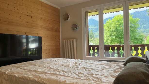 Un dormitorio con una cama grande, un televisor, un ventanal con vistas a las montañas y una pared de madera.