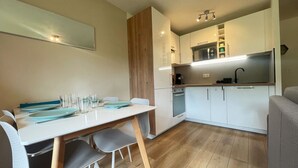 Una cocina moderna con armarios blancos, horno empotrado y microondas. Cuenta con una mesa de comedor con sillas y una pequeña isla de cocina.