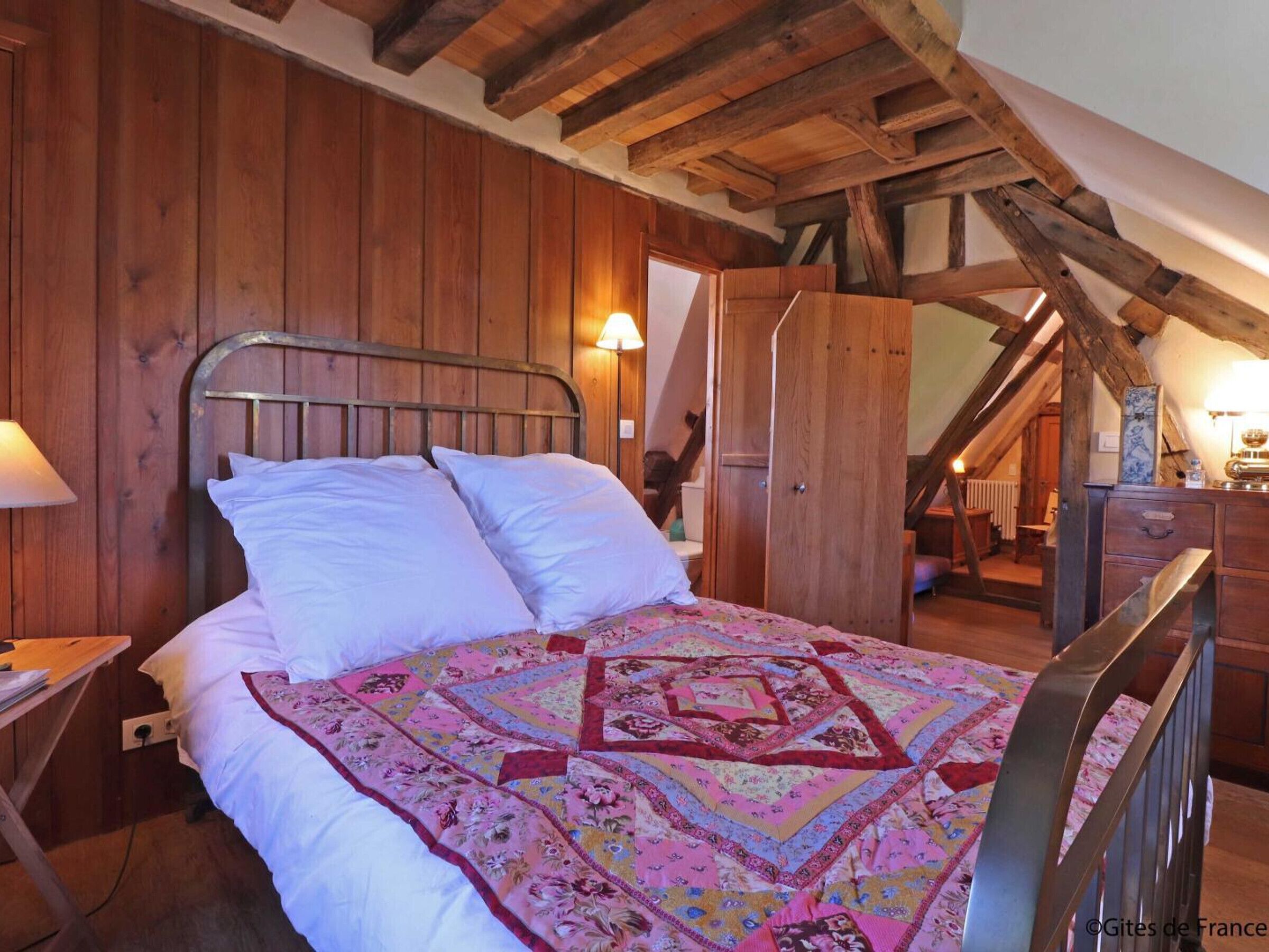 A bedroom with a wooden ceiling, a metal bed frame, and a colorful quilt.
