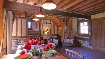 Een rustieke eetruimte met een houten tafel gedekt voor vier personen, een vaas rode tulpen en een trap naar een hoger gelegen verdieping.