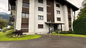 A multi-story building with a modern architectural design, featuring a combination of white and dark wood paneling, multiple windows, and a covered entrance area.