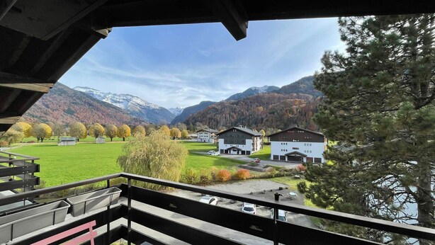 A balcony with a view of a mountainous landscape, a lake, and a building with a parking area.