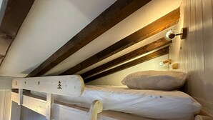 A bunk bed with a wooden ladder, a single bed below, and a wall-mounted light fixture.