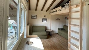 A cozy room with a bunk bed, a sofa, a small table, and a window with a view of the outside.