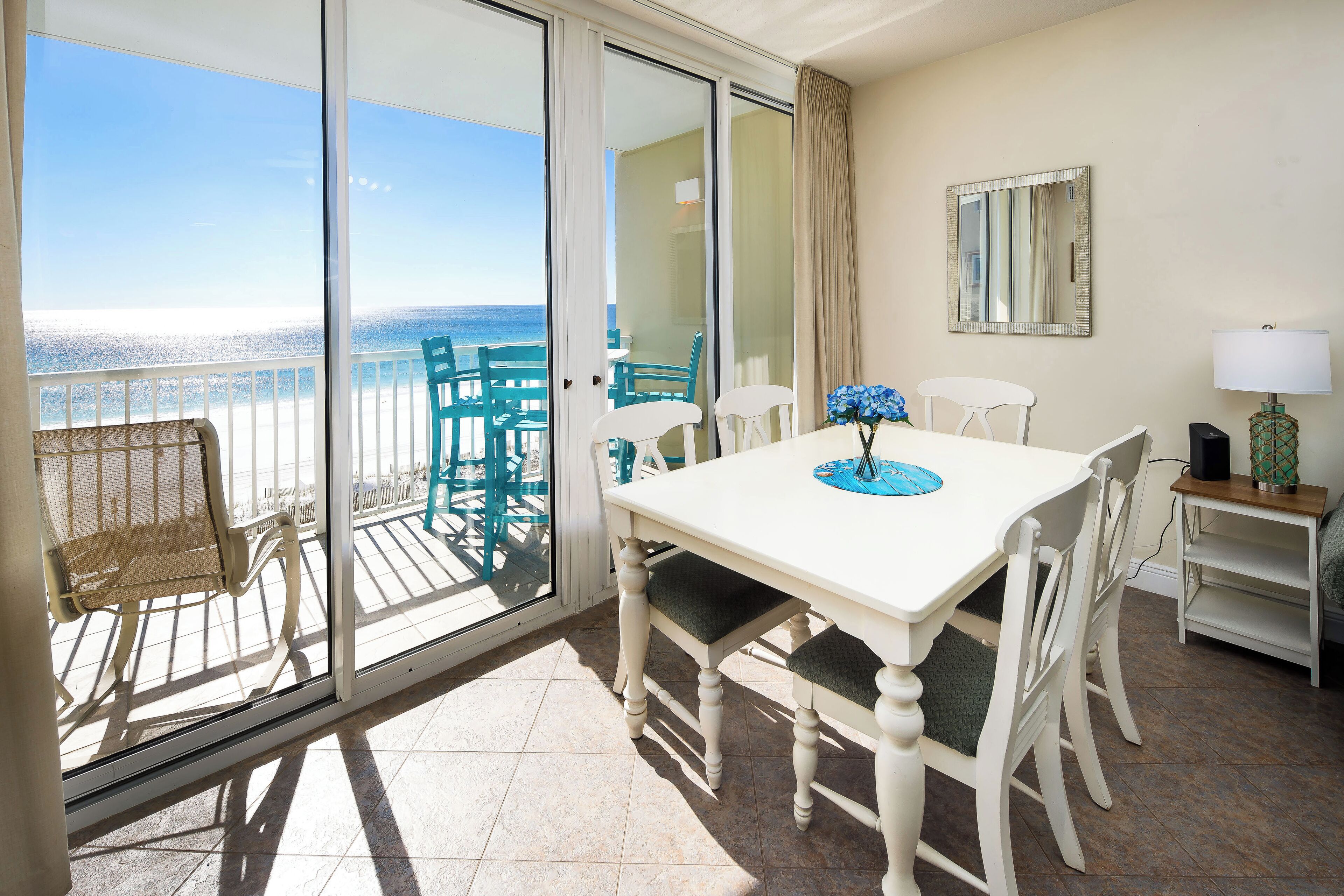 A balcony with a view of the ocean, a white table with chairs, and a small side table with a lamp.