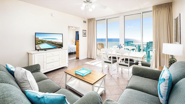 Un soggiorno moderno con una televisione grande, un'area pranzo e un balcone vista mare.