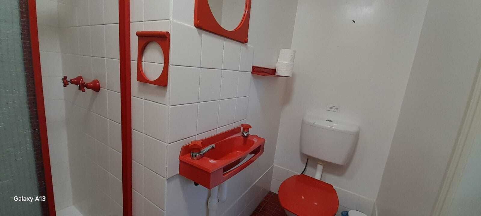 A bathroom with white tiled walls, a red toilet, a red sink, and a red toilet paper holder.