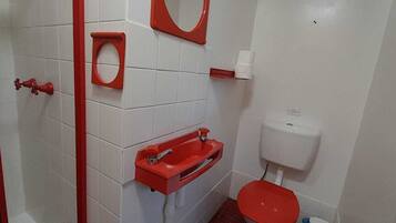 A bathroom with white tiled walls, a red toilet, a red sink, and a red toilet paper holder.