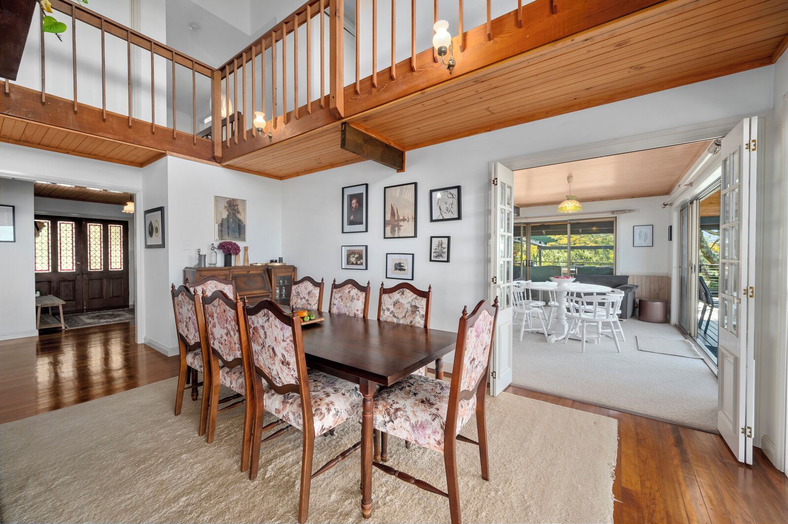 Una sala da pranzo con tavolo in legno e sedie floreali, una scala e vista sull'esterno.