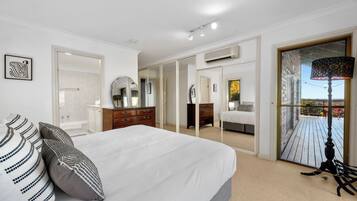 A bedroom with a large bed, a dresser, a mirror, and a view of a balcony with outdoor scenery.