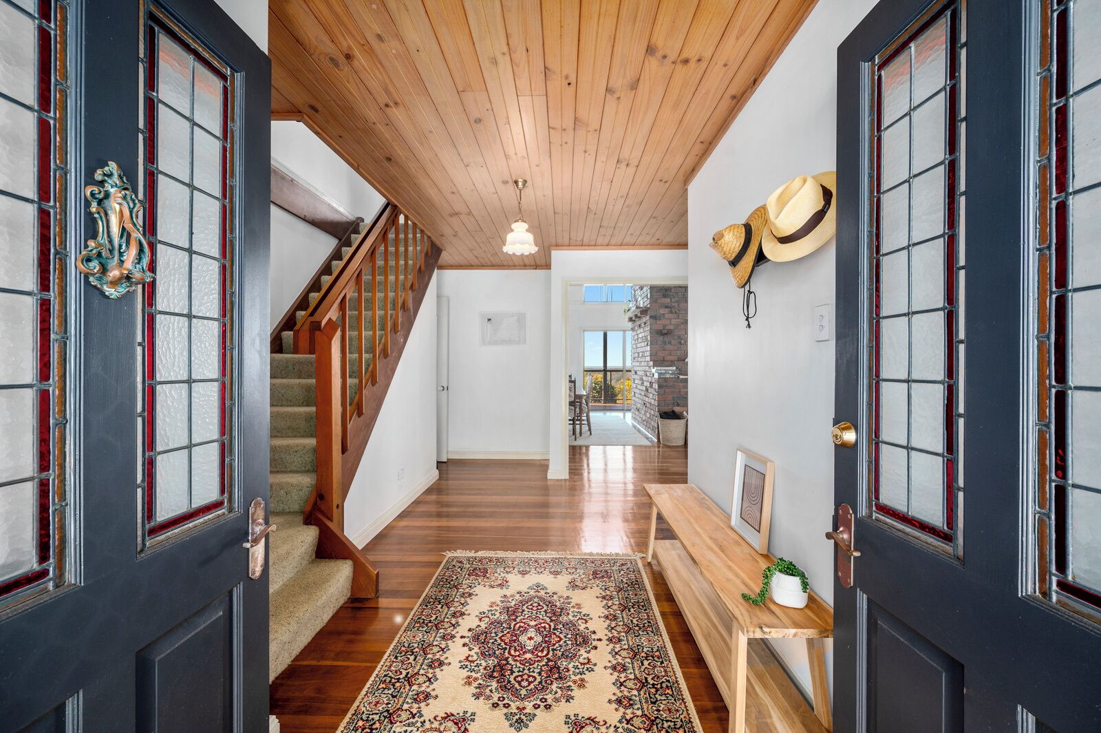 Un couloir avec un plafond en bois, un escalier, un tapis à motifs et un banc.