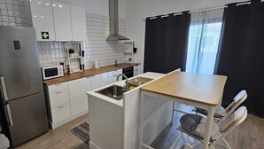 Une cuisine compacte avec des meubles blancs, un réfrigérateur en acier inoxydable, un four à micro-ondes et un évier.