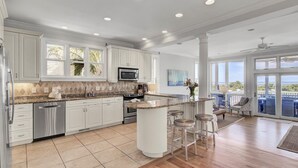 A spacious kitchen with white cabinets, a granite countertop, and a large island with bar stools. - Oceanfront, Beachfront & Golf Views | 4BR in Ocean Point (Isle of Palms)