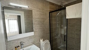 A modern bathroom with a glass-enclosed shower, a white sink with a mirror above, and a toilet with a roll of toilet paper on top. - Noa Ayvalık Guest House (Ayvalik)