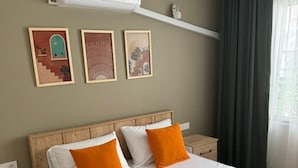 A neatly made bed with white and orange bedding, a wooden headboard, and a wall-mounted air conditioner. - Noa Ayvalık Guest House (Ayvalik)