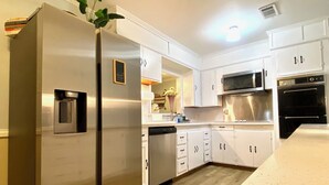 A modern kitchen with white cabinetry, stainless steel appliances, and a wooden floor. - Gulfport Beach Home By Casino (Gulfport)