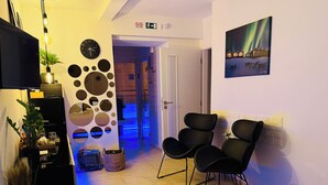 Habitación de hotel con cama, dos sillas negras, un reloj de pared, un cuadro y una planta.