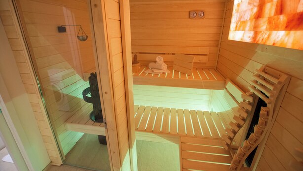 Una sauna con paredes y bancos de madera, una puerta de cristal y un pequeño reloj en la pared.
