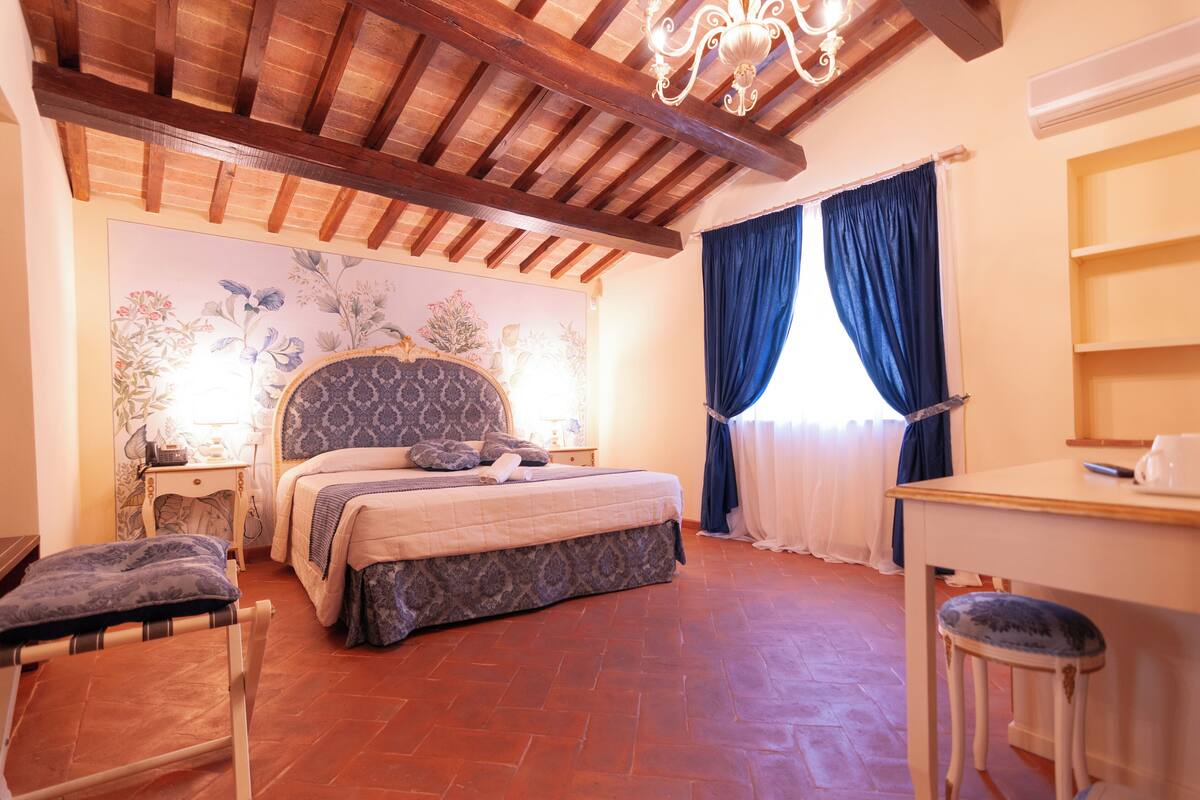 A bedroom with a bed, a desk, a chair, a window with curtains, and a wooden ceiling.