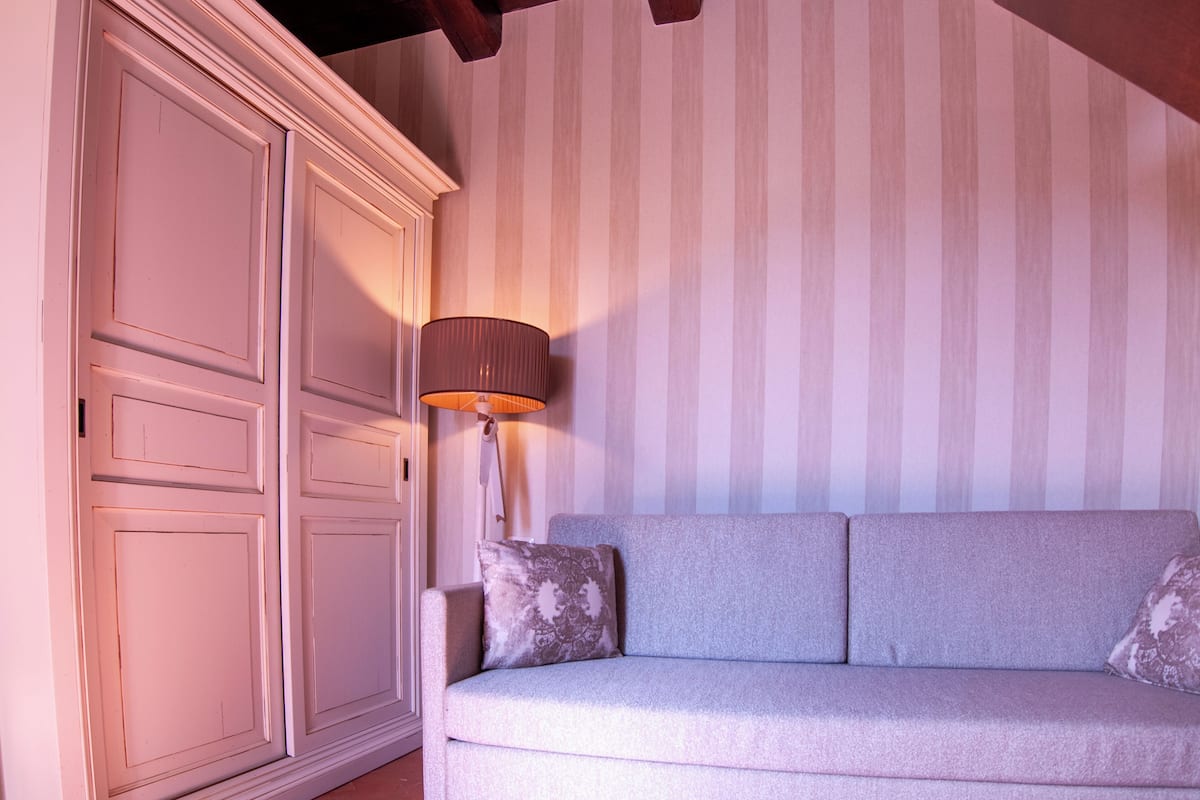 A room with a striped wallpaper, a white cabinet, and a grey sofa with patterned cushions.