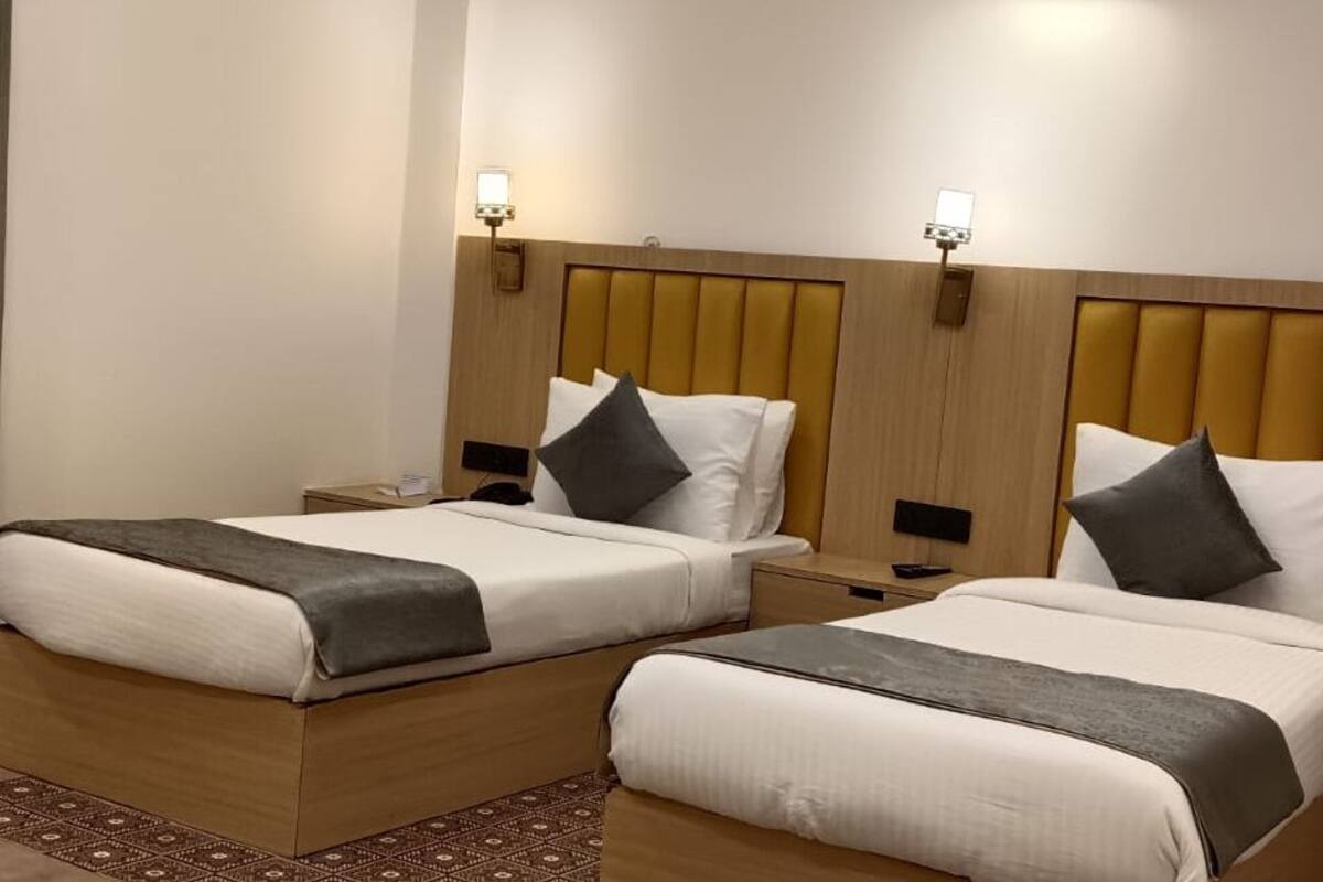 Une chambre d’hôtel avec deux lits, chacun doté d’une tête de lit en bois, de tables de chevet et de lampes fixées au mur.