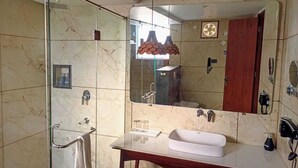 A bathroom with a glass-enclosed shower, a marble-tiled wall, a wooden vanity with a sink, and a large mirror.