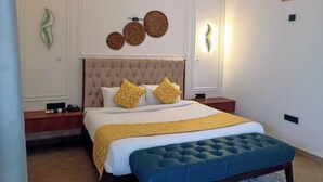 A bedroom with a tufted headboard, a large bed with yellow and white bedding, a blue bench, and decorative wall art.