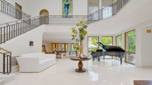 A spacious, well-lit living area with a grand piano, a white sofa, and a large potted plant.
