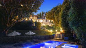 A swimming pool with lounge chairs and umbrellas, surrounded by trees and a stone wall.