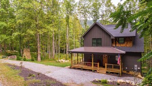 Eine Holzhütte mit überdachter Veranda, einer Steinmauer und einem Wald im Hintergrund.