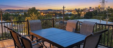 Una terraza con mesa y sillas, con vista a un paisaje urbano al atardecer.